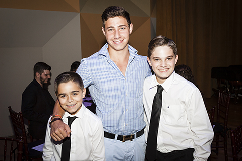 A man in a blue dress shirt poses with two kids at an event